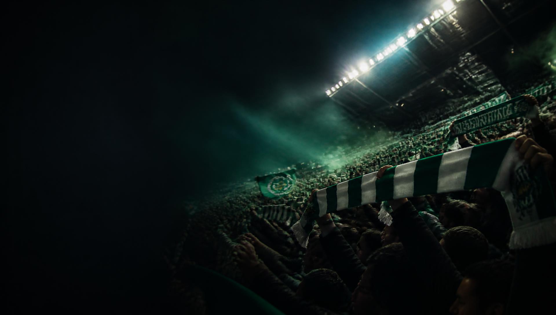 Supporters raising club scarves on a floodlit terrace